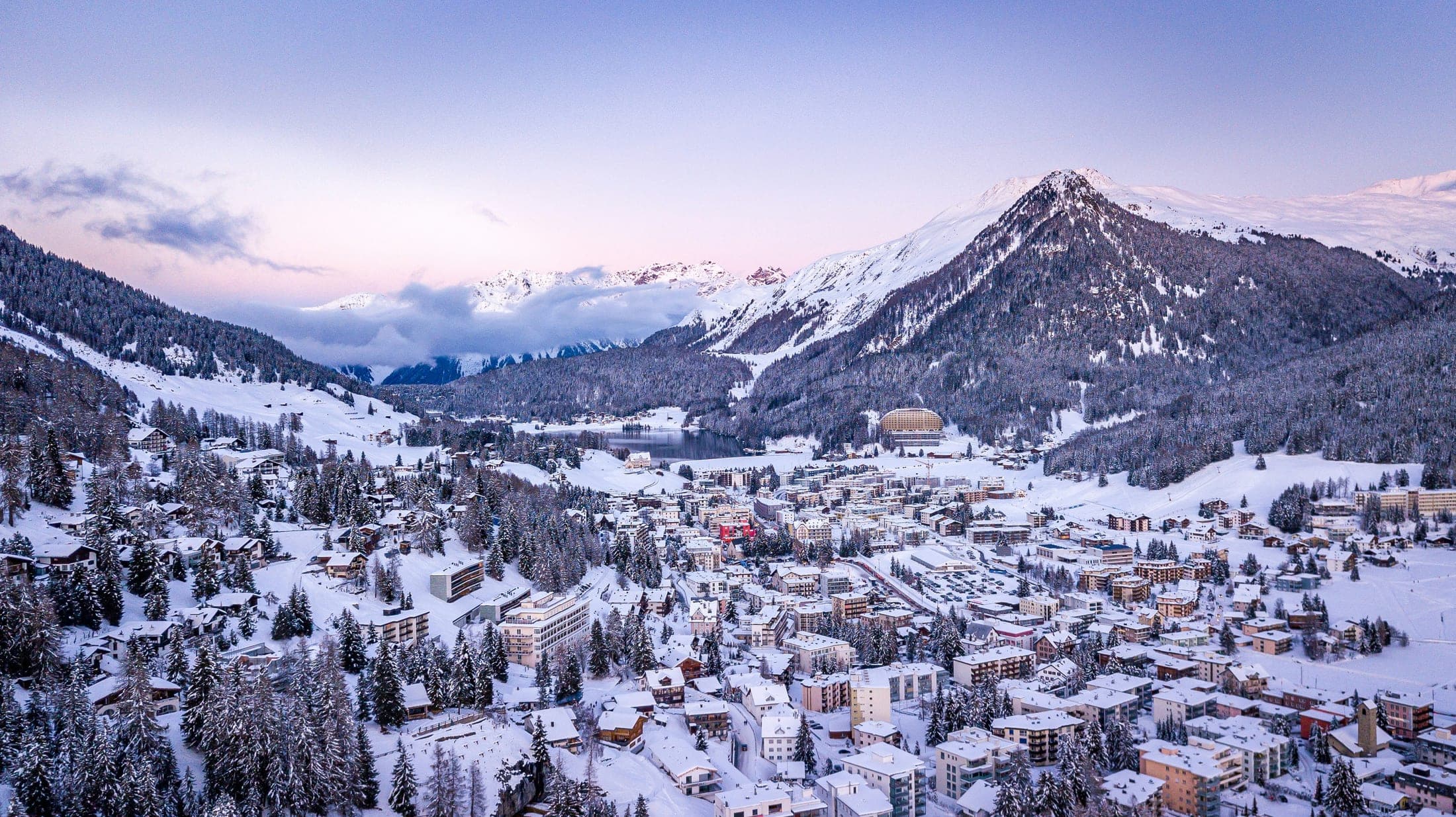 The town of Davos under snow at dusk, with the surrounding peaks behind it
