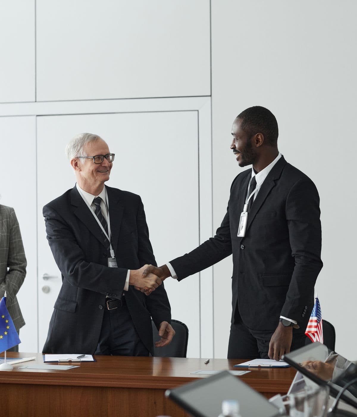 Two delegates shaking hands across a conference table set with flags and papers