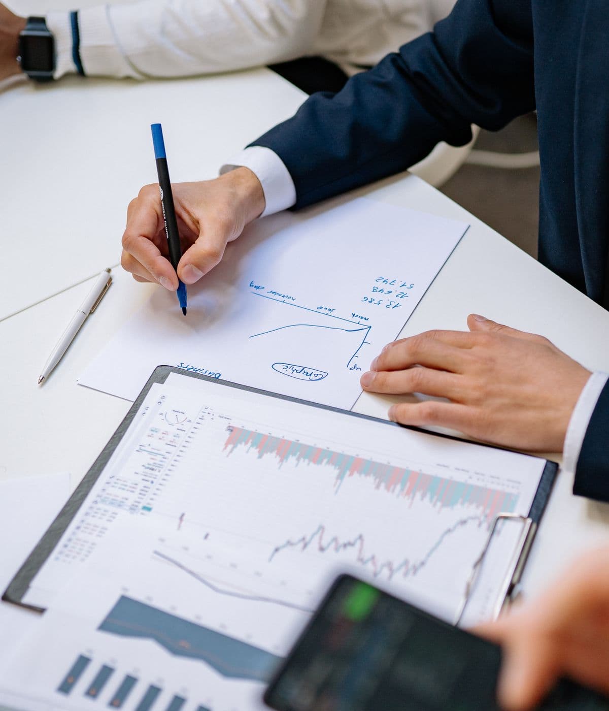 Financial charts and reports spread across a desk as two people review them