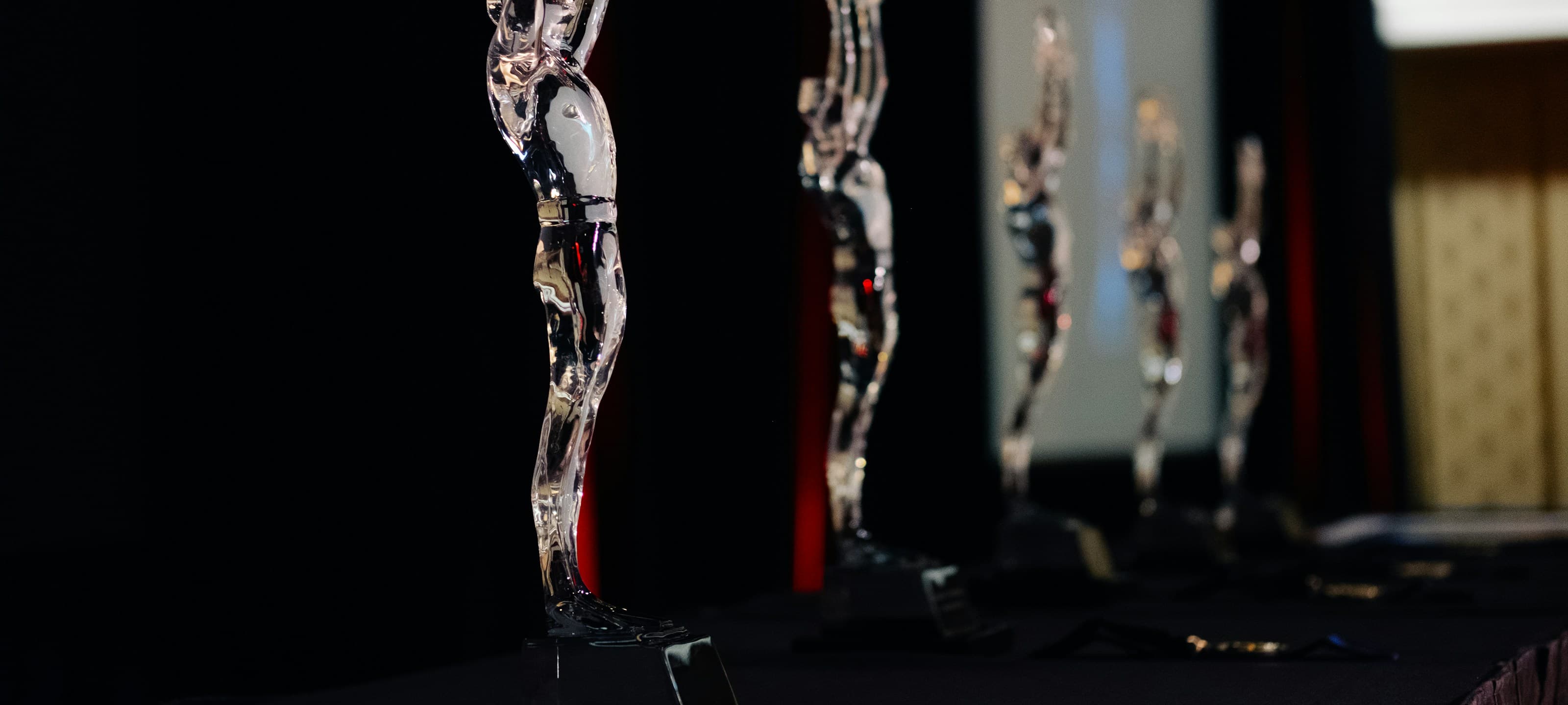A row of crystal award statuettes on a dark stage with a warm curtain glow