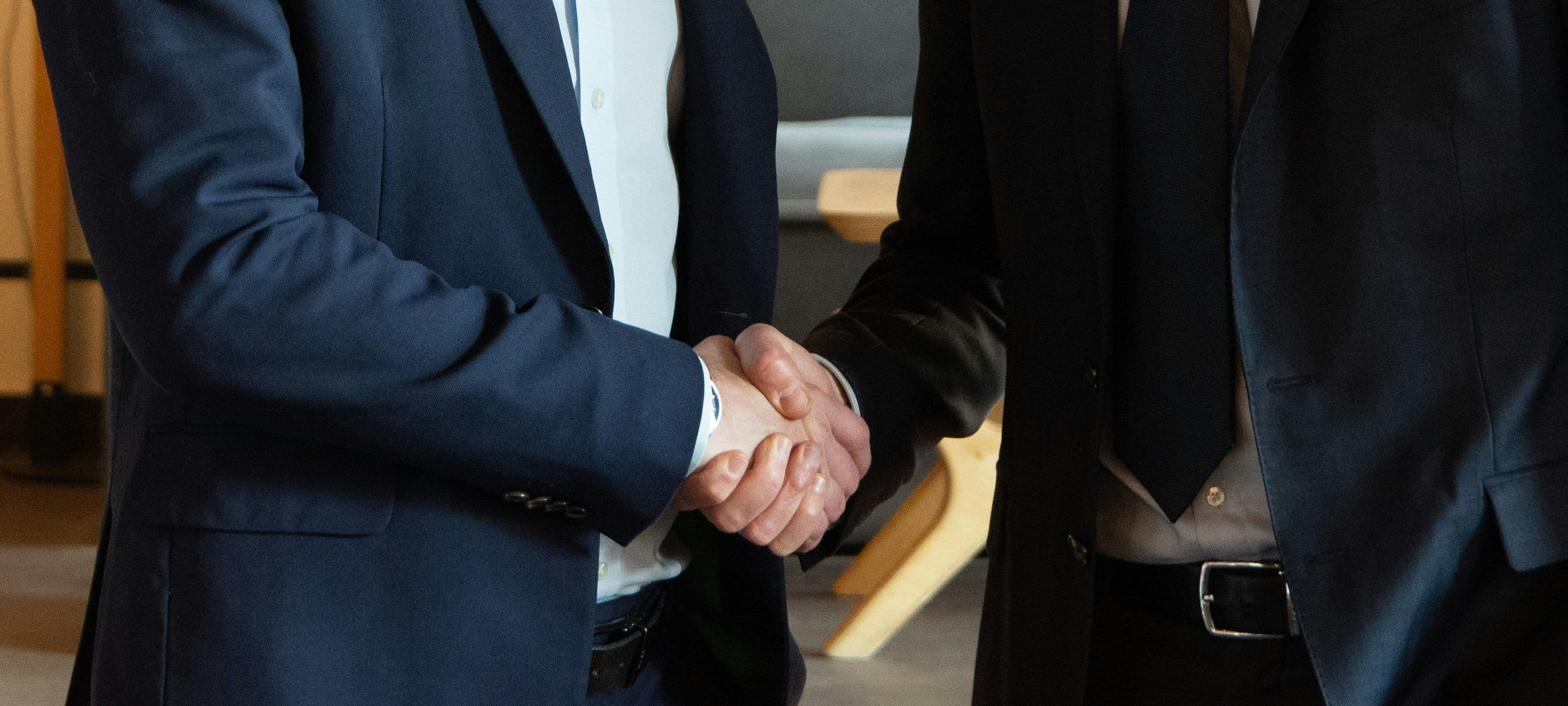 A close view of two business leaders in navy suits shaking hands in agreement