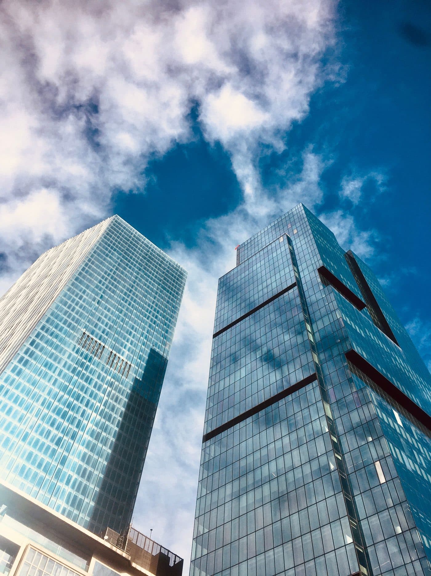 Looking up at glass financial-district towers converging against a bright blue sky