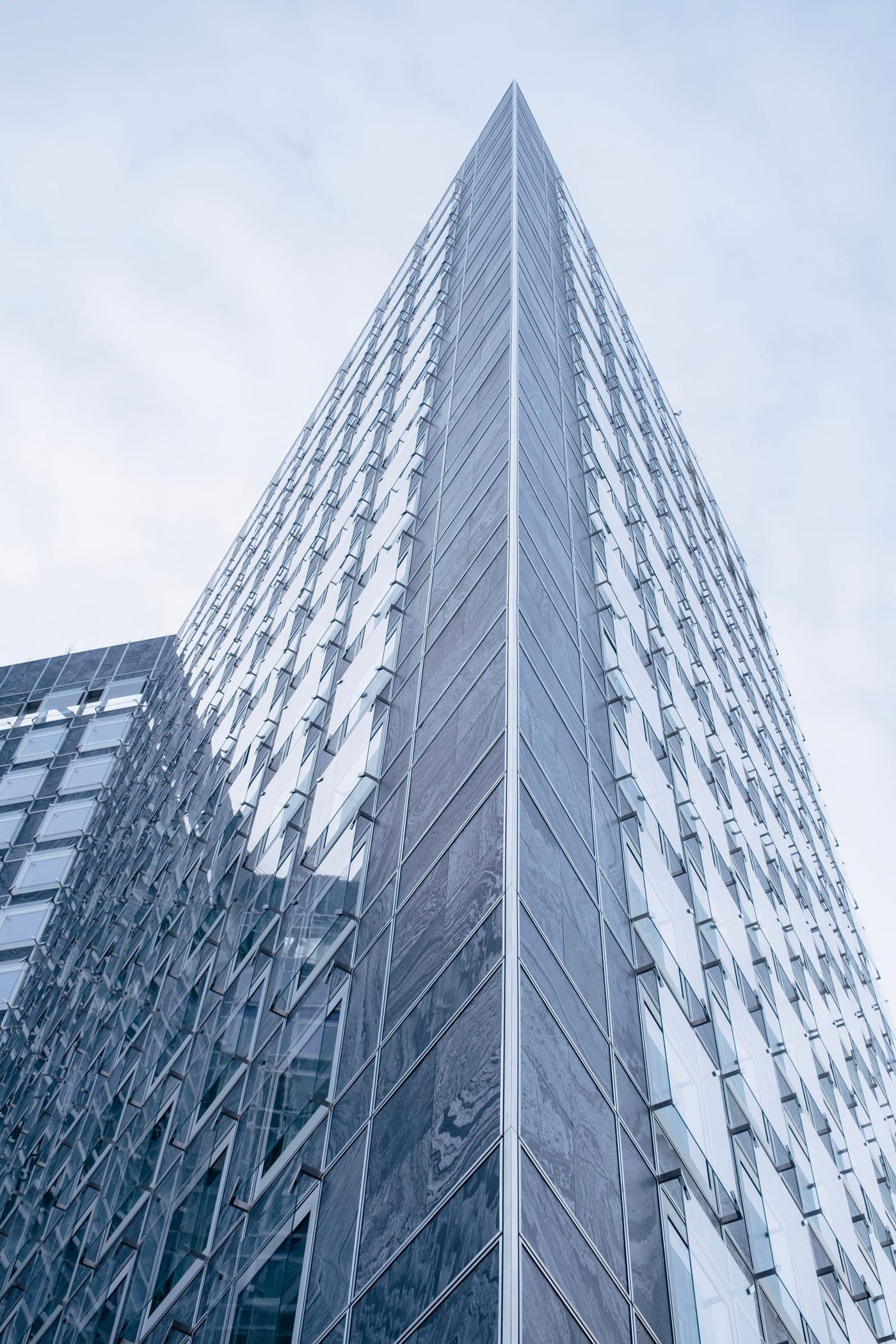 Looking straight up the converging glass facade of a high-rise office tower against a pale sky